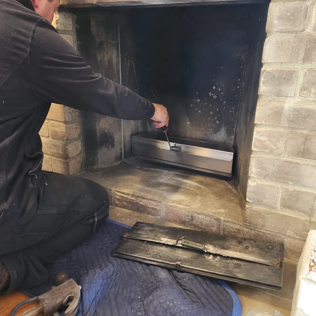Technician installing a new stainless steel clean-out door in a fireplace