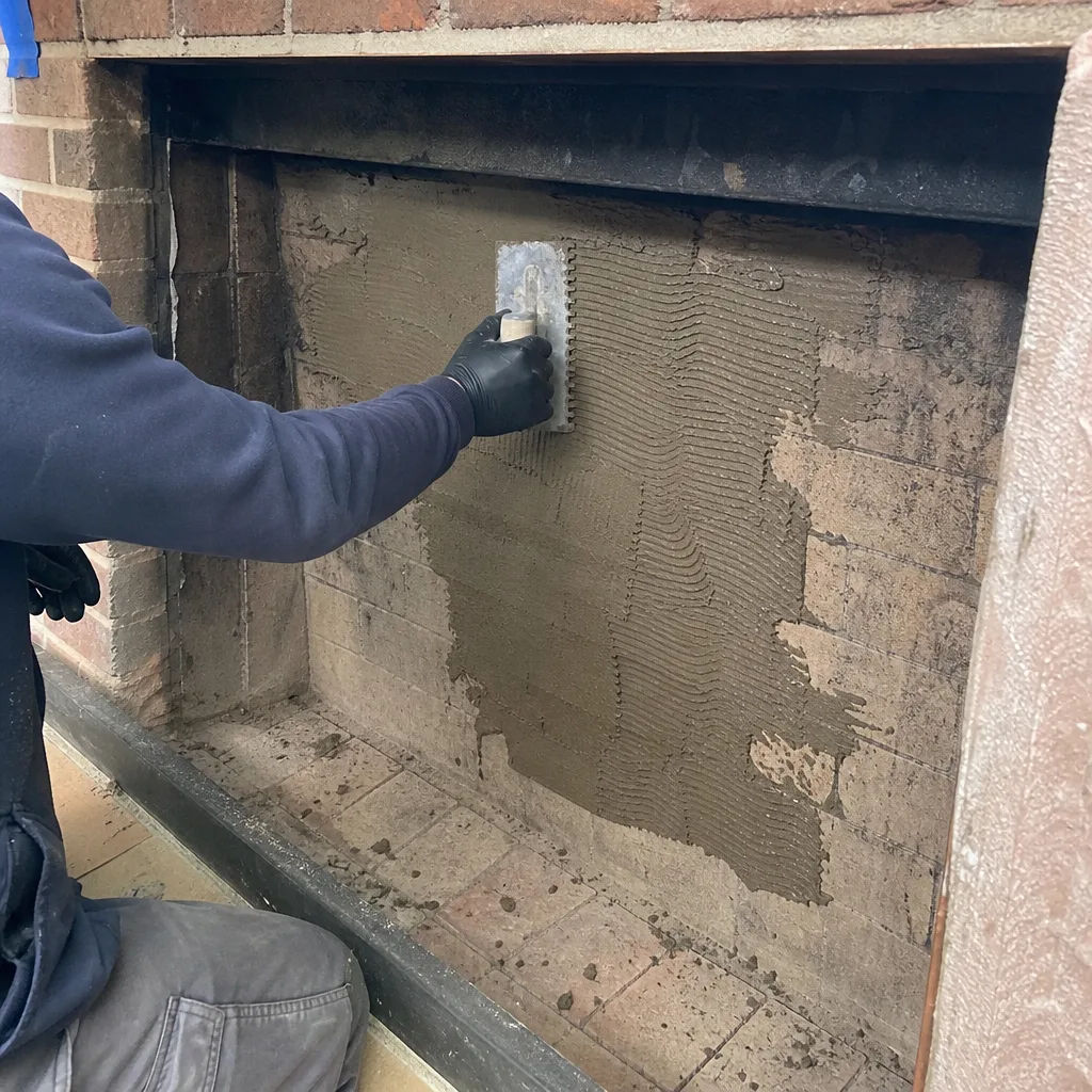 Professional fireplace technician applying mortar to firebox brick during restoration.